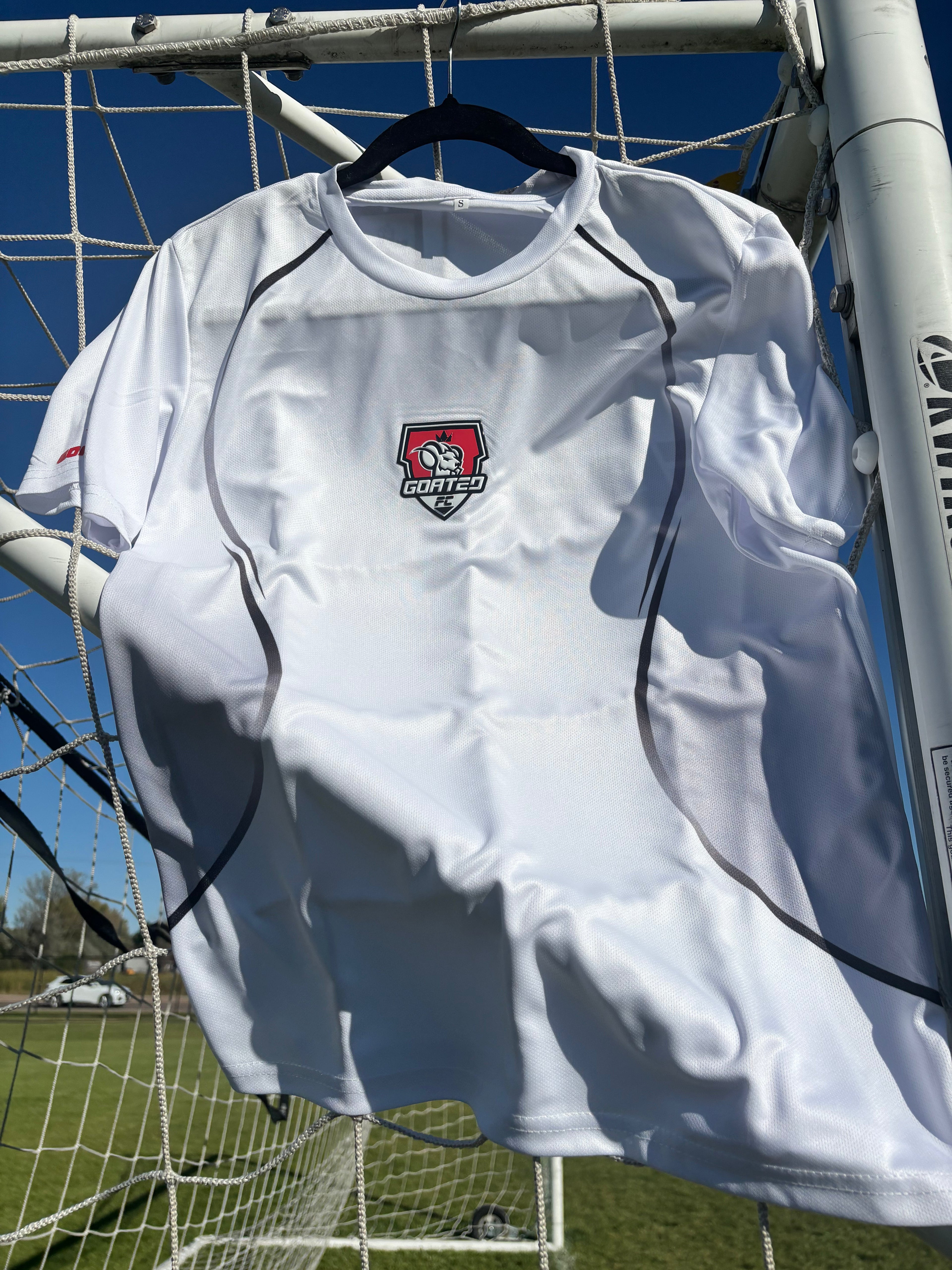 GOATED FC white training jersey hanging on a soccer goal